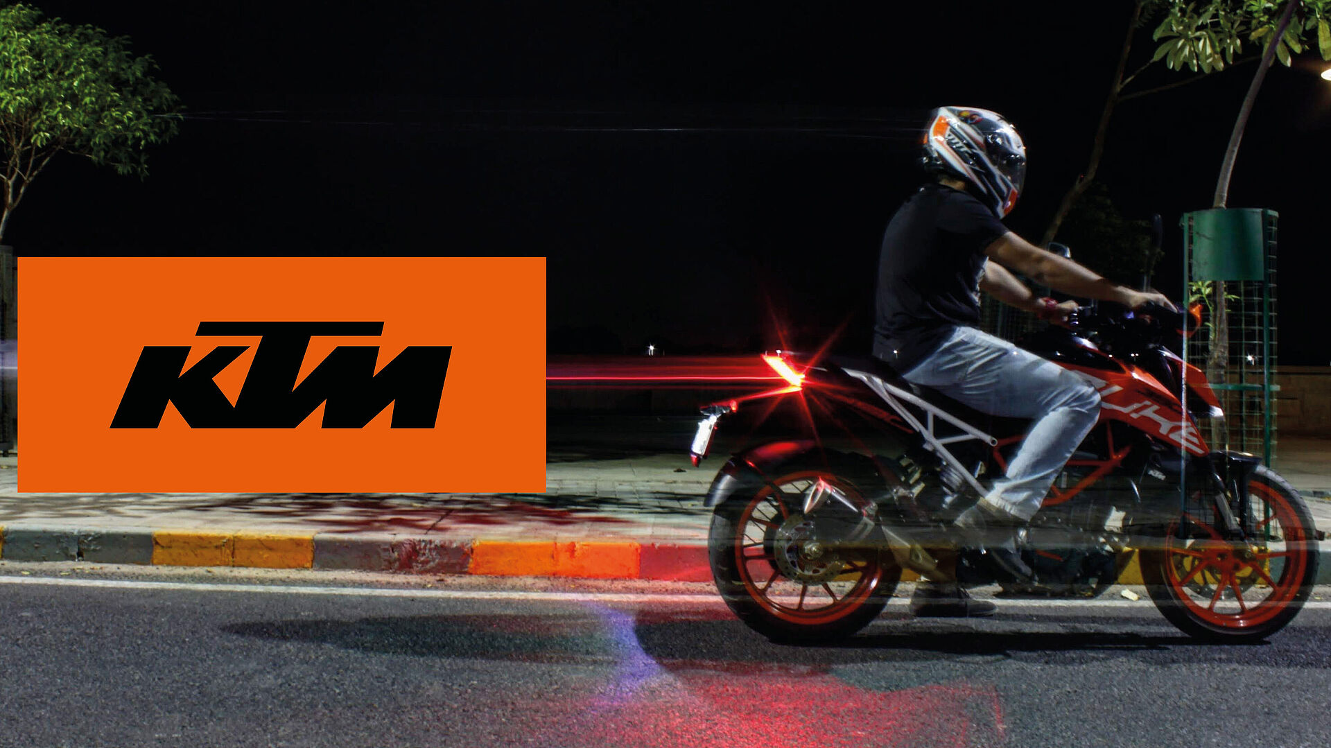 Fahrer mit Helm auf einem KTM Motorrad bei Nacht. Links KTM Logo