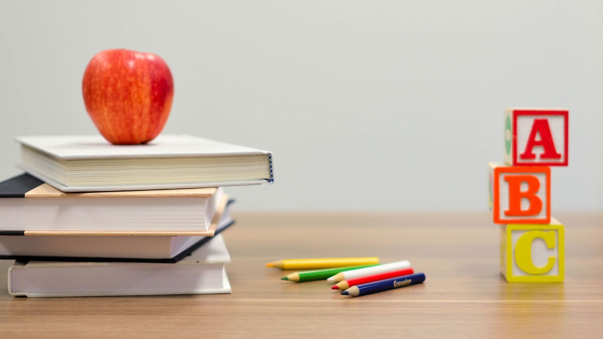 Pult in einem Klassenzimmer auf welchem Bücher, ein Apfel und Buchstabenbausteine liegen